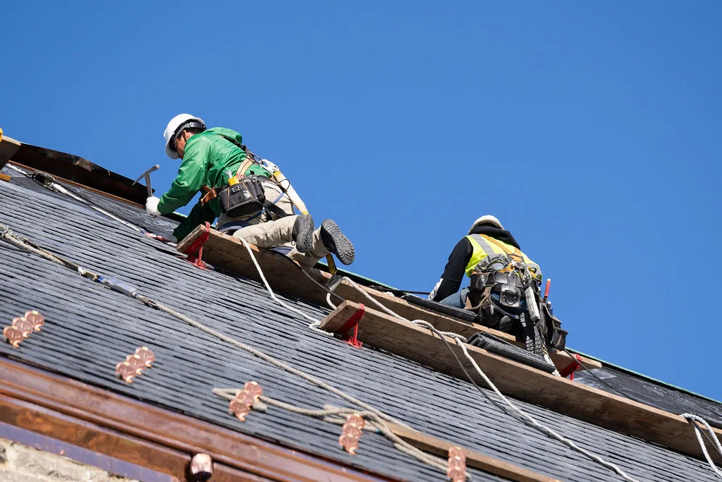 Two roofers setting slate on the steep pitch