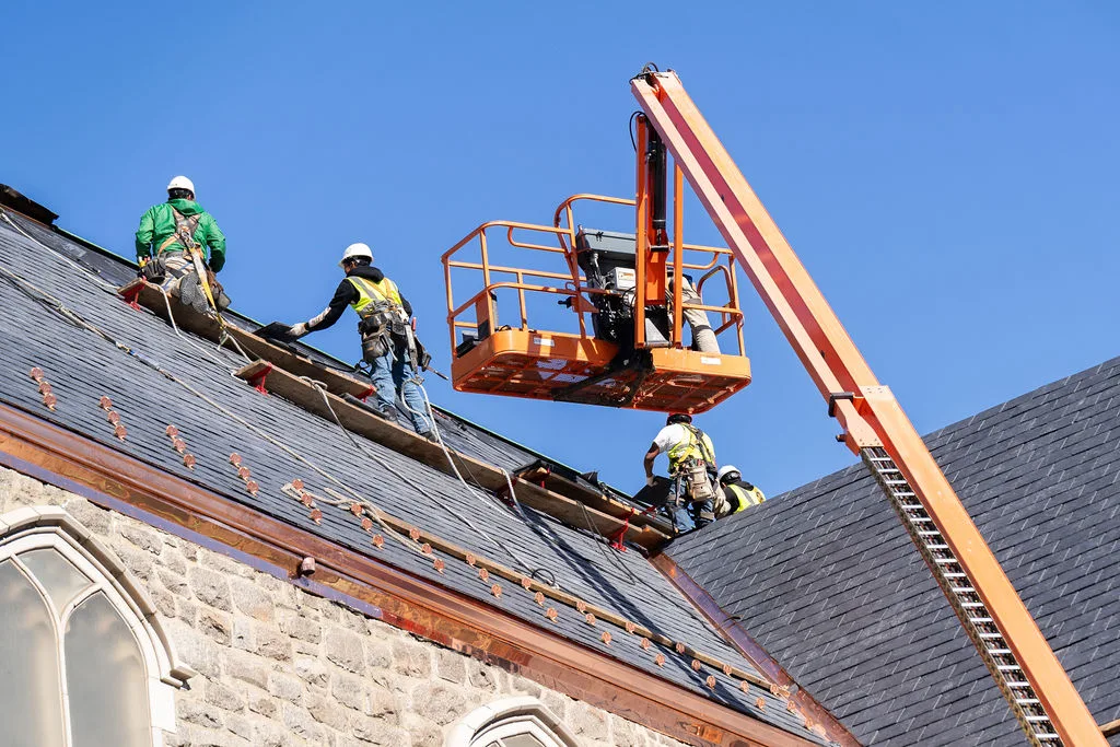 Roofers working from an aerial lift at the ridge of the slate roof